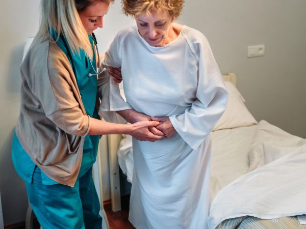 Female caregiver helping elderly female patient to stand up